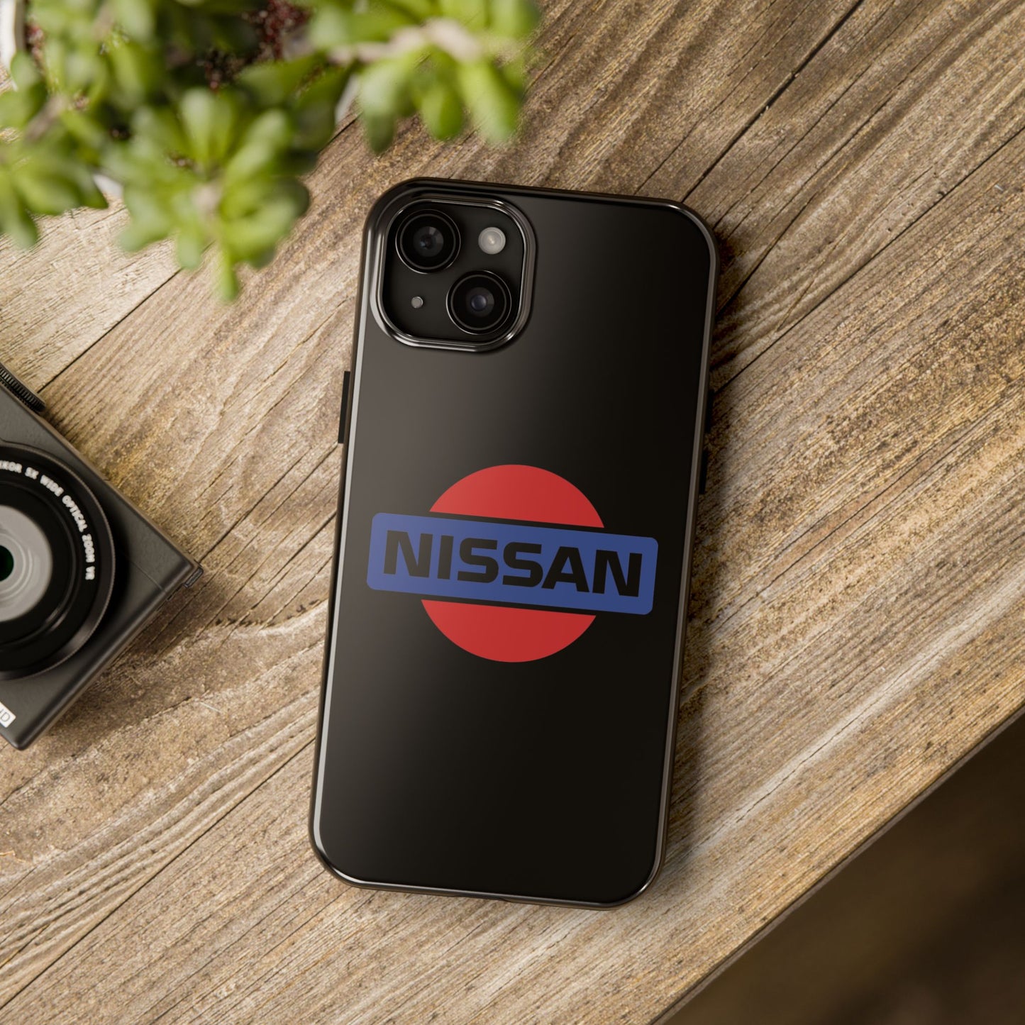 Black iPhone 15 Plus Vintage Nissan phone case on a table with accessories.