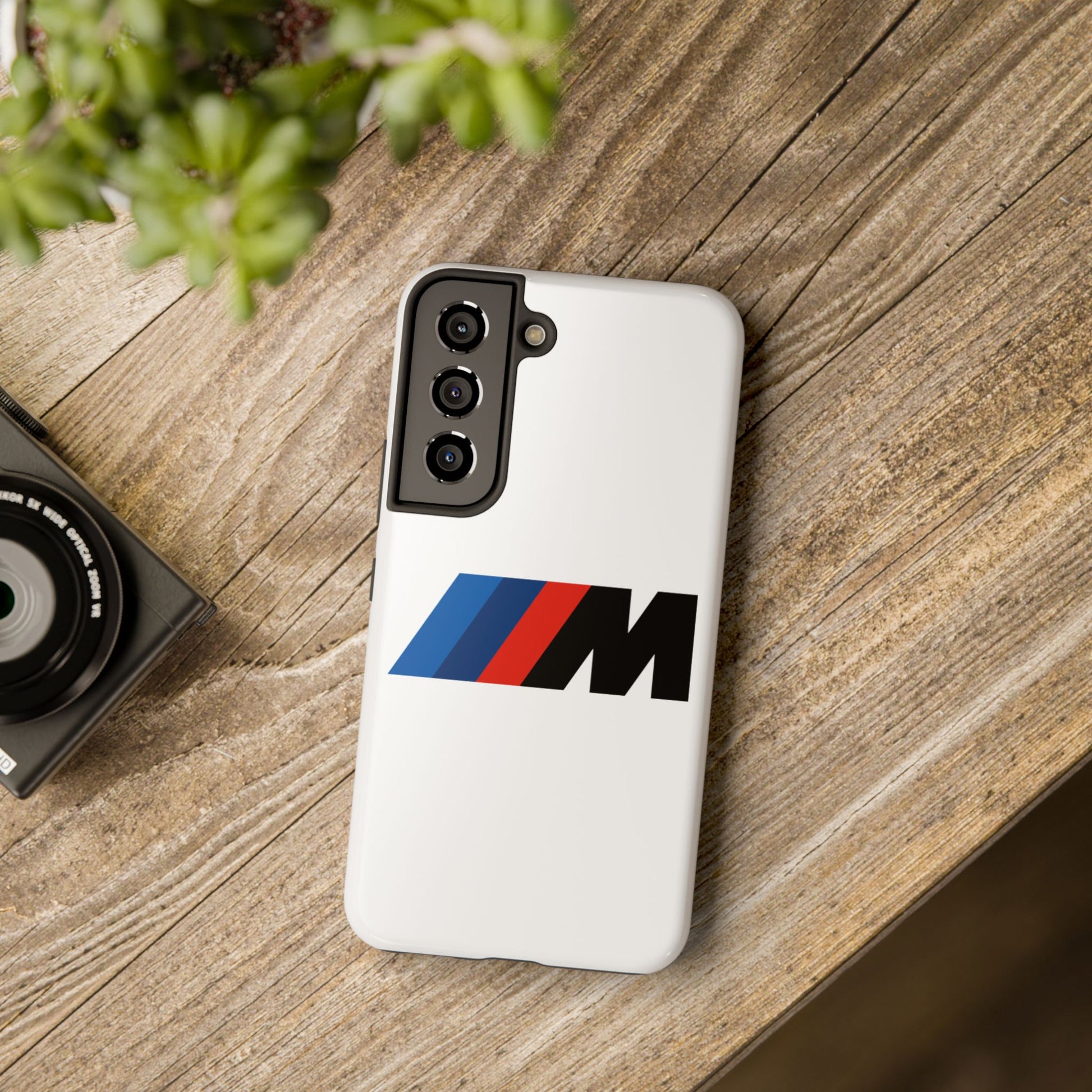 White Samsung Galaxy S22 BMW M phone case on a table with accessories.