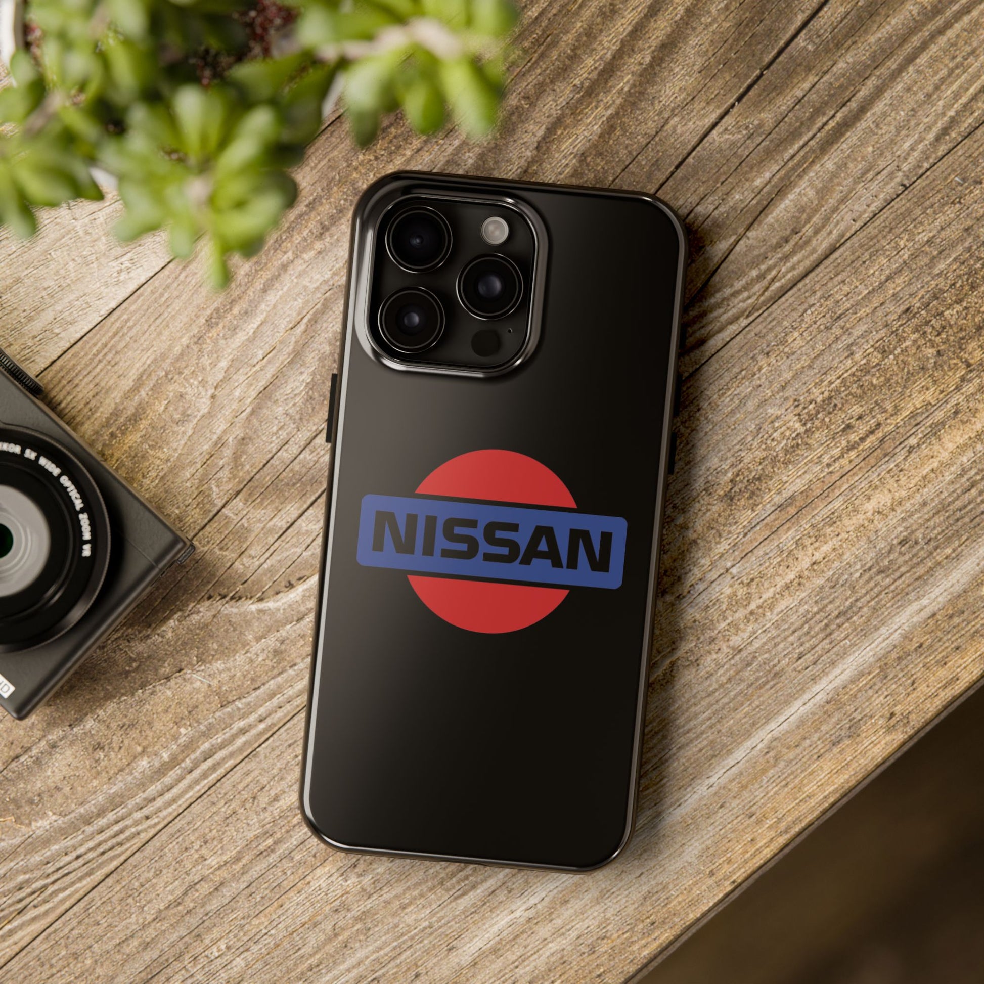 Black iPhone 15 Pro Max Vintage Nissan phone case on a table with accessories.