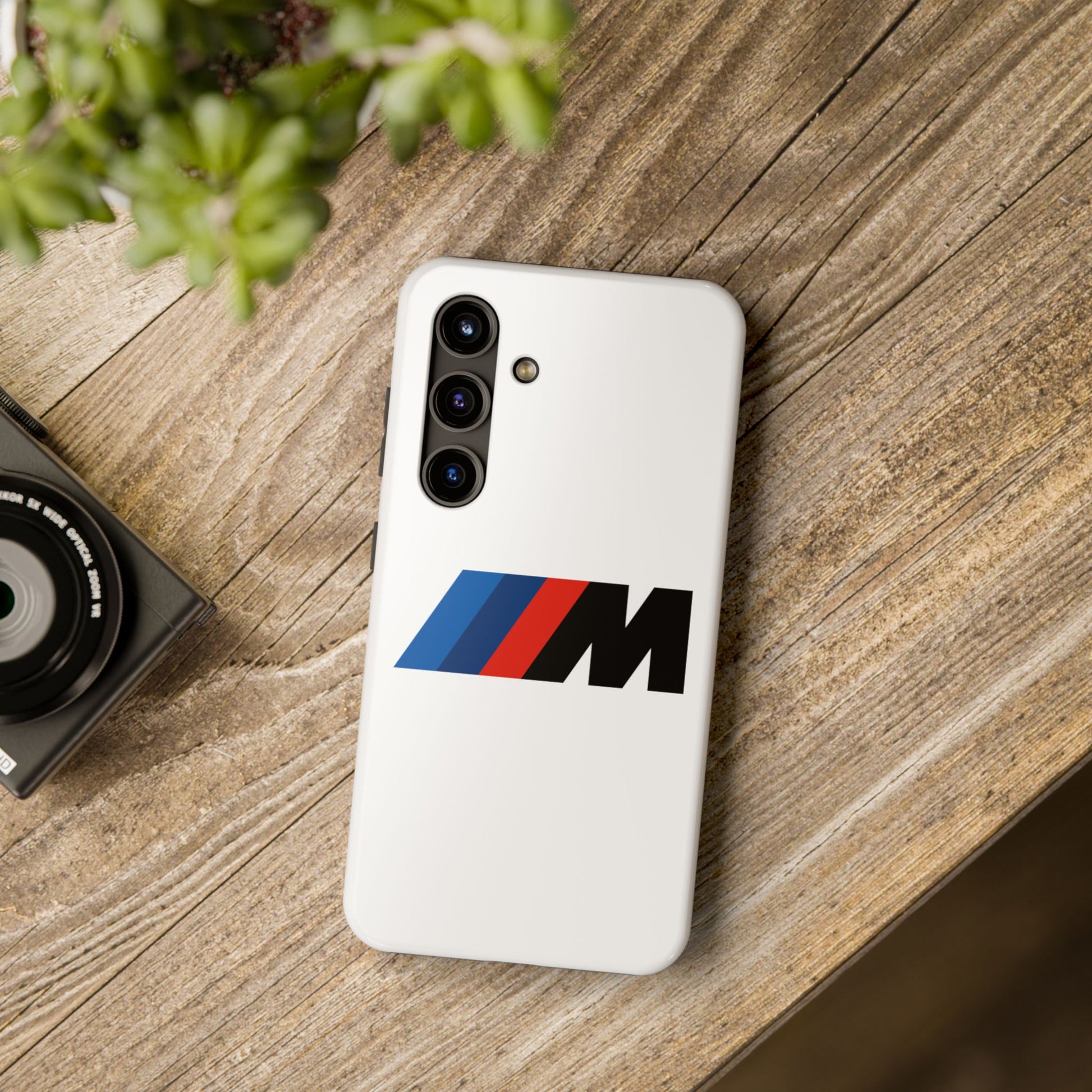 White Samsung Galaxy S24 BMW M phone case on a table with accessories.