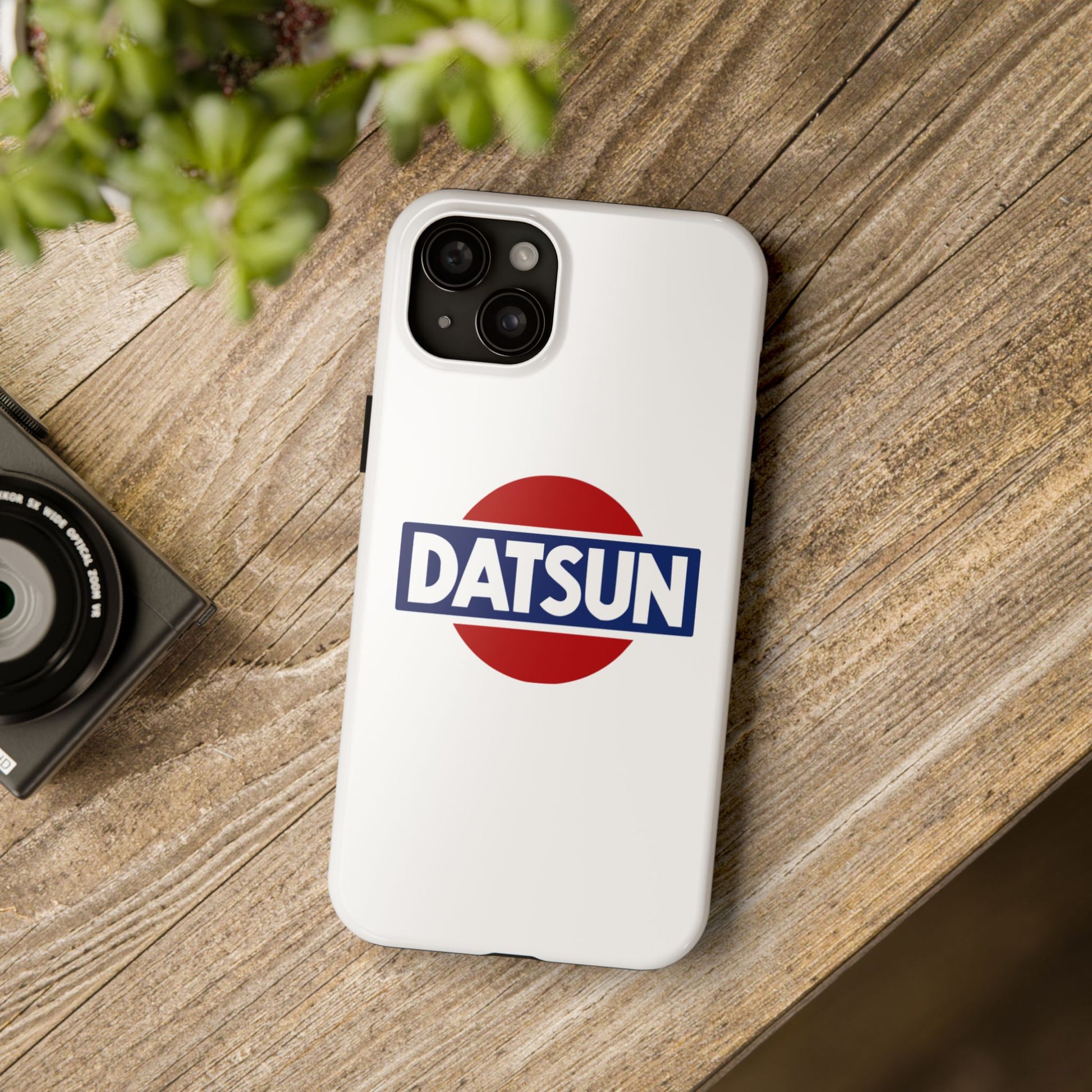 White iPhone 15 Plus Datsun phone case on a table with accessories.