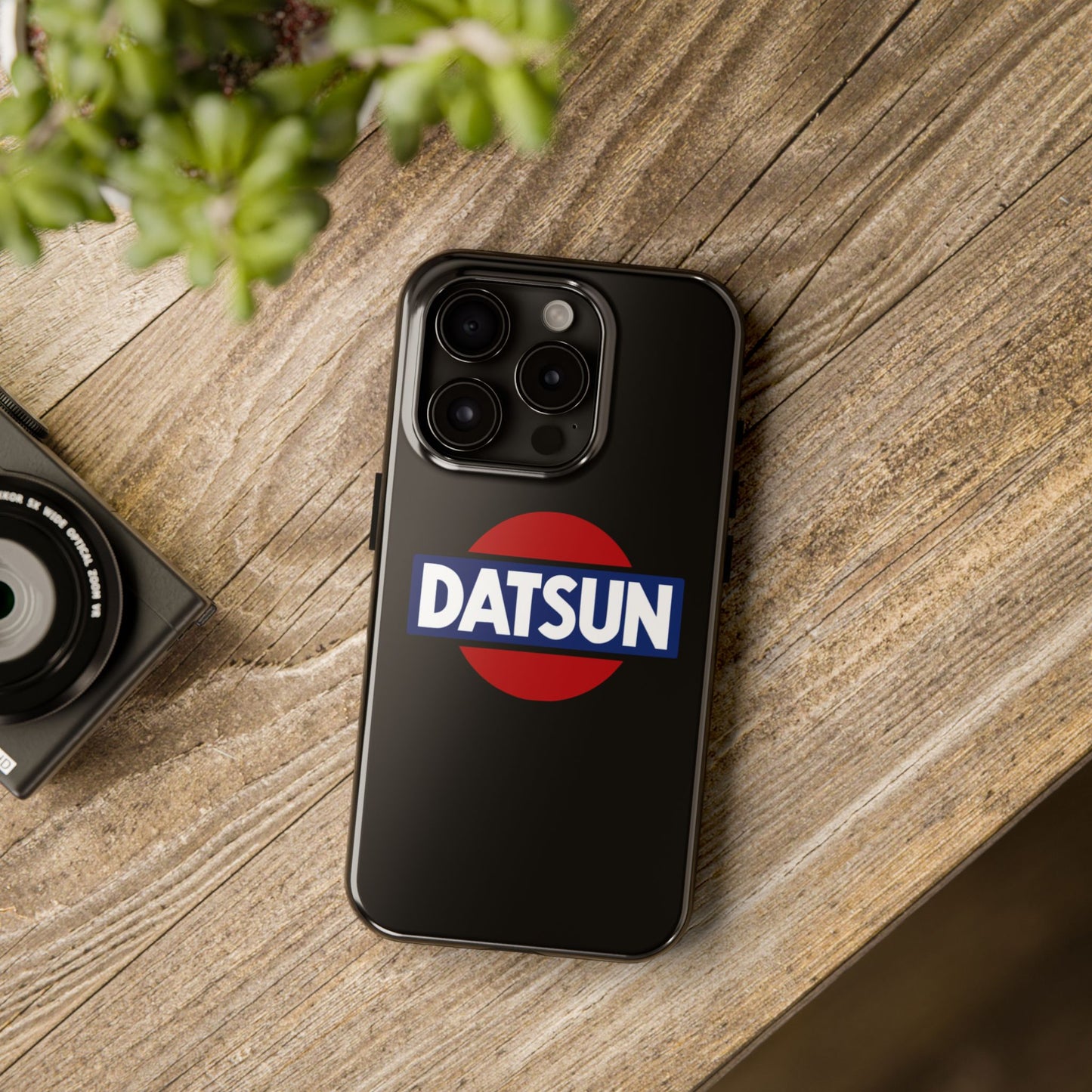 Black iPhone 15 Pro Datsun phone case on a table with accessories.