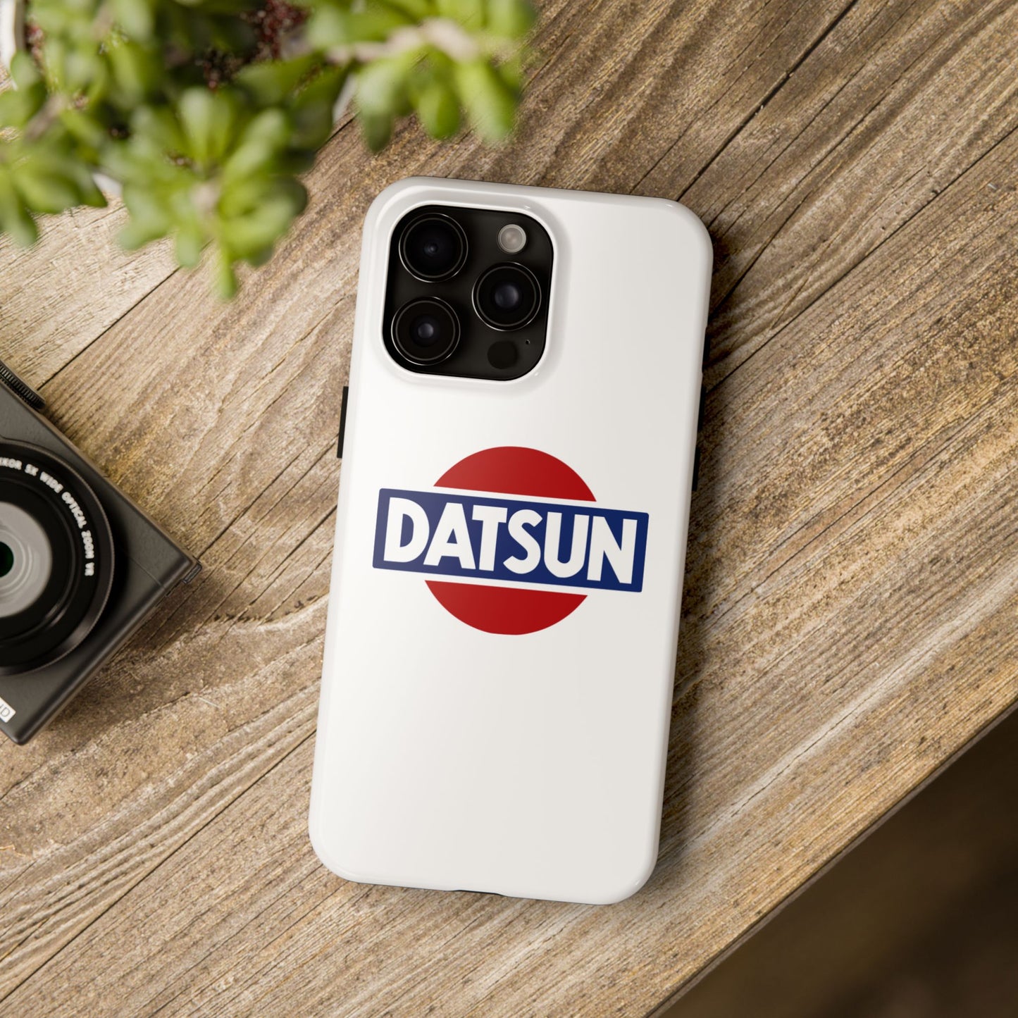 White iPhone 15 Pro Max Datsun phone case on a table with accessories.