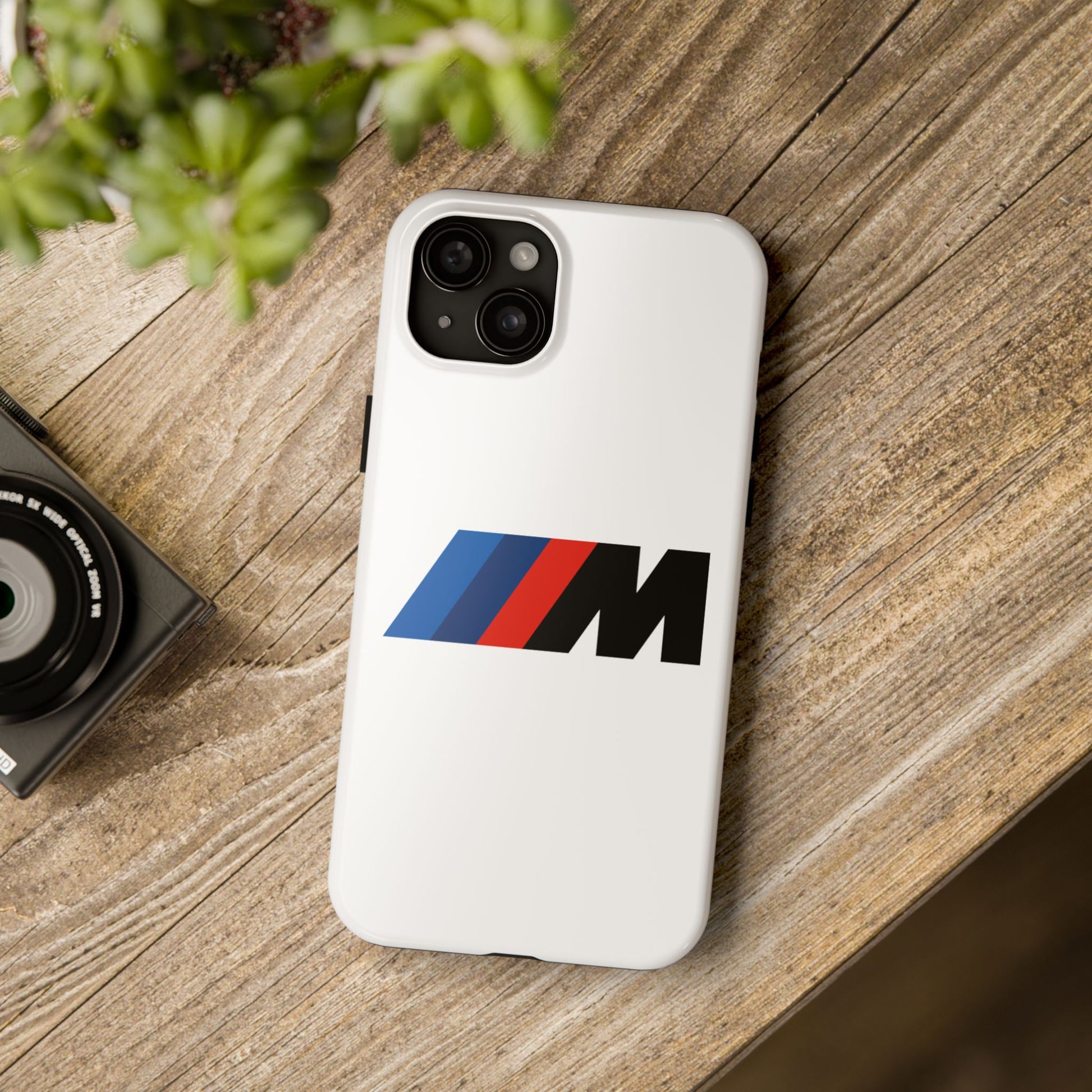 White iPhone 15 Plus BMW M phone case on a table with accessories.