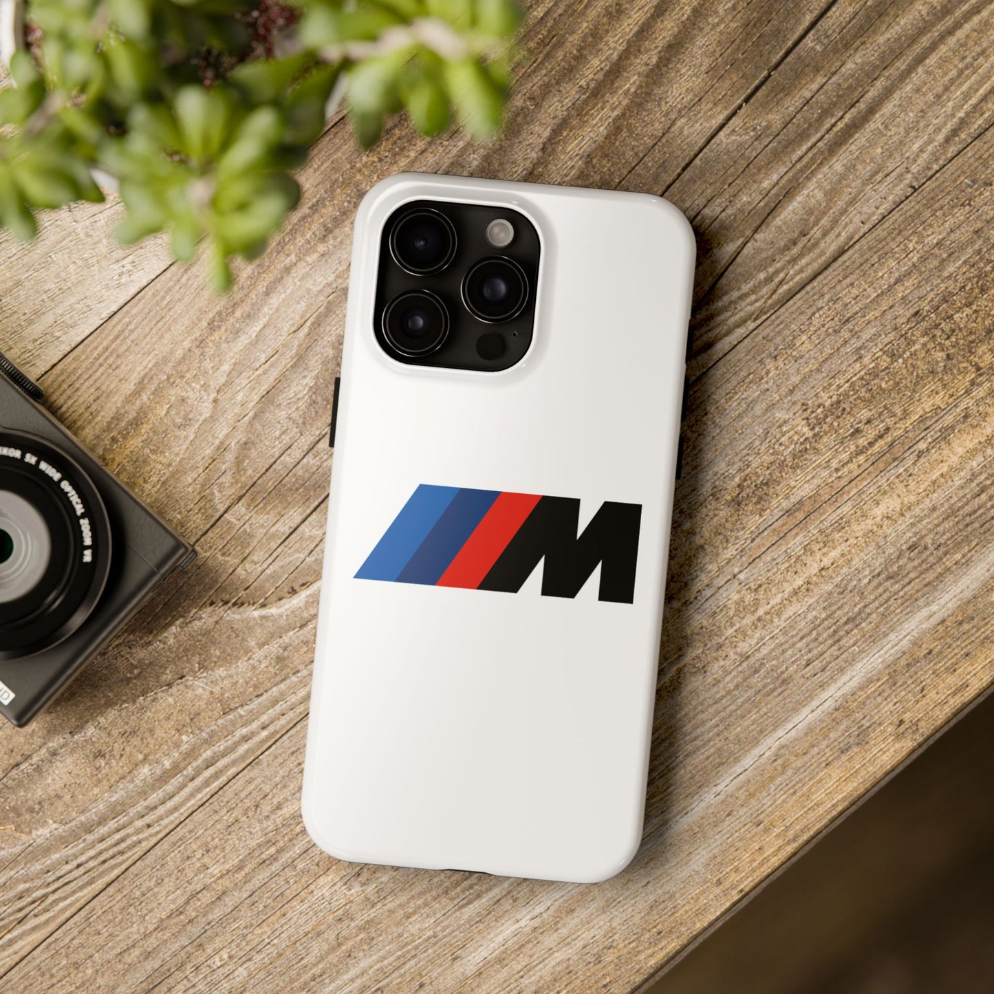 White iPhone 15 Pro Max BMW M phone case on a table with accessories.