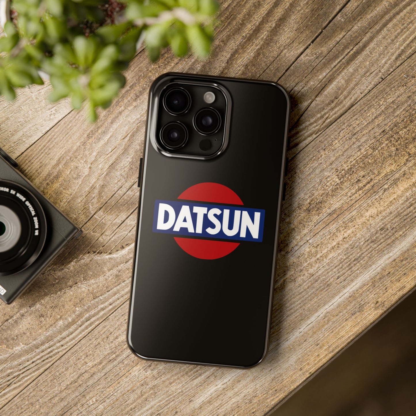 Black iPhone 15 Pro Max Datsun phone case on a table with accessories.