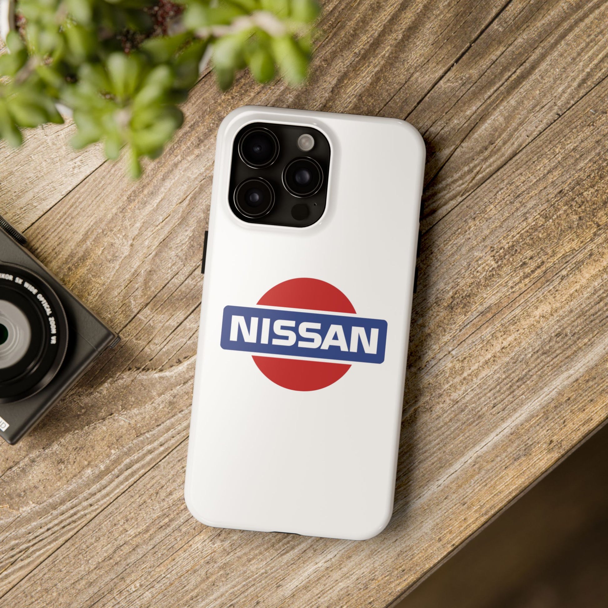 White iPhone 15 Pro Max Vintage Nissan phone case on a table with accessories.