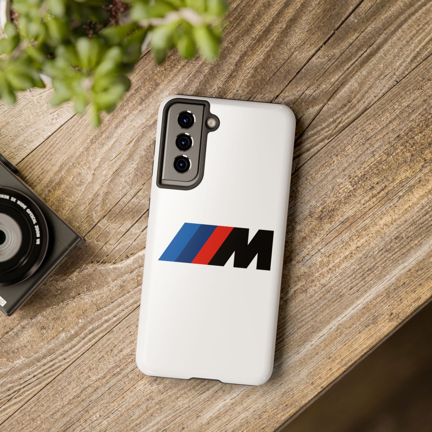 White Samsung Galaxy S21 BMW M phone case on a table with accessories.