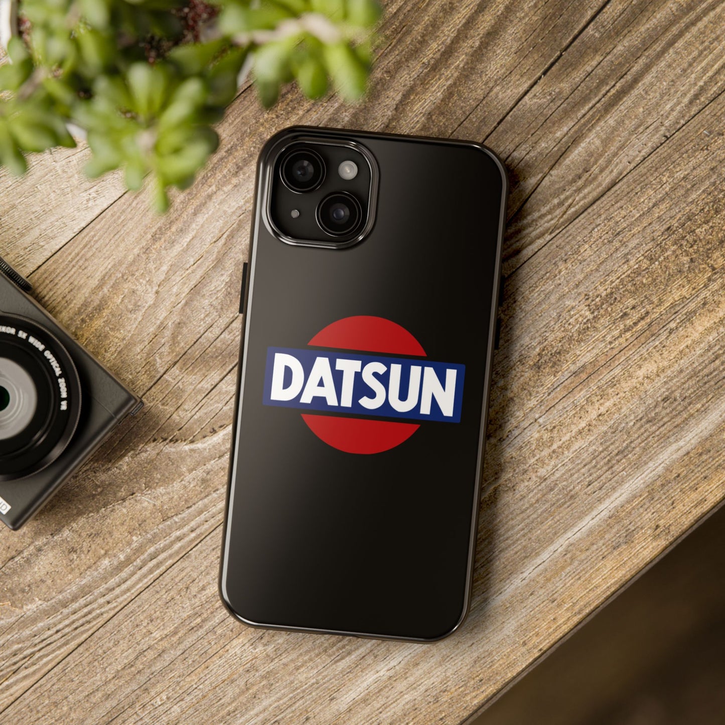 Black iPhone 15 Plus Datsun phone case on a table with accessories.