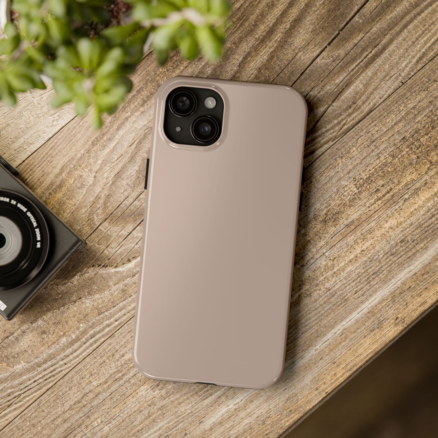 iPhone 15 Plus Aston Martin Arizona Bronze phone case on a table with accessories. 