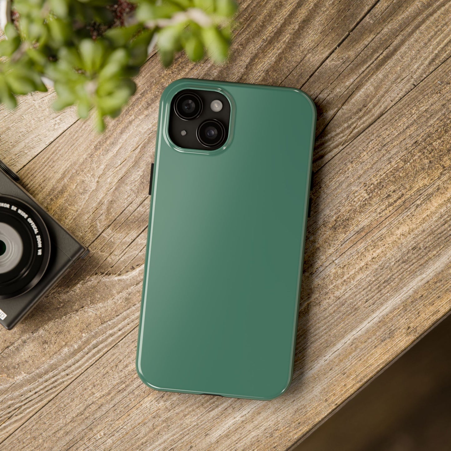 iPhone 15 Plus Aston Martin Racing Green phone case on a table with accessories. 