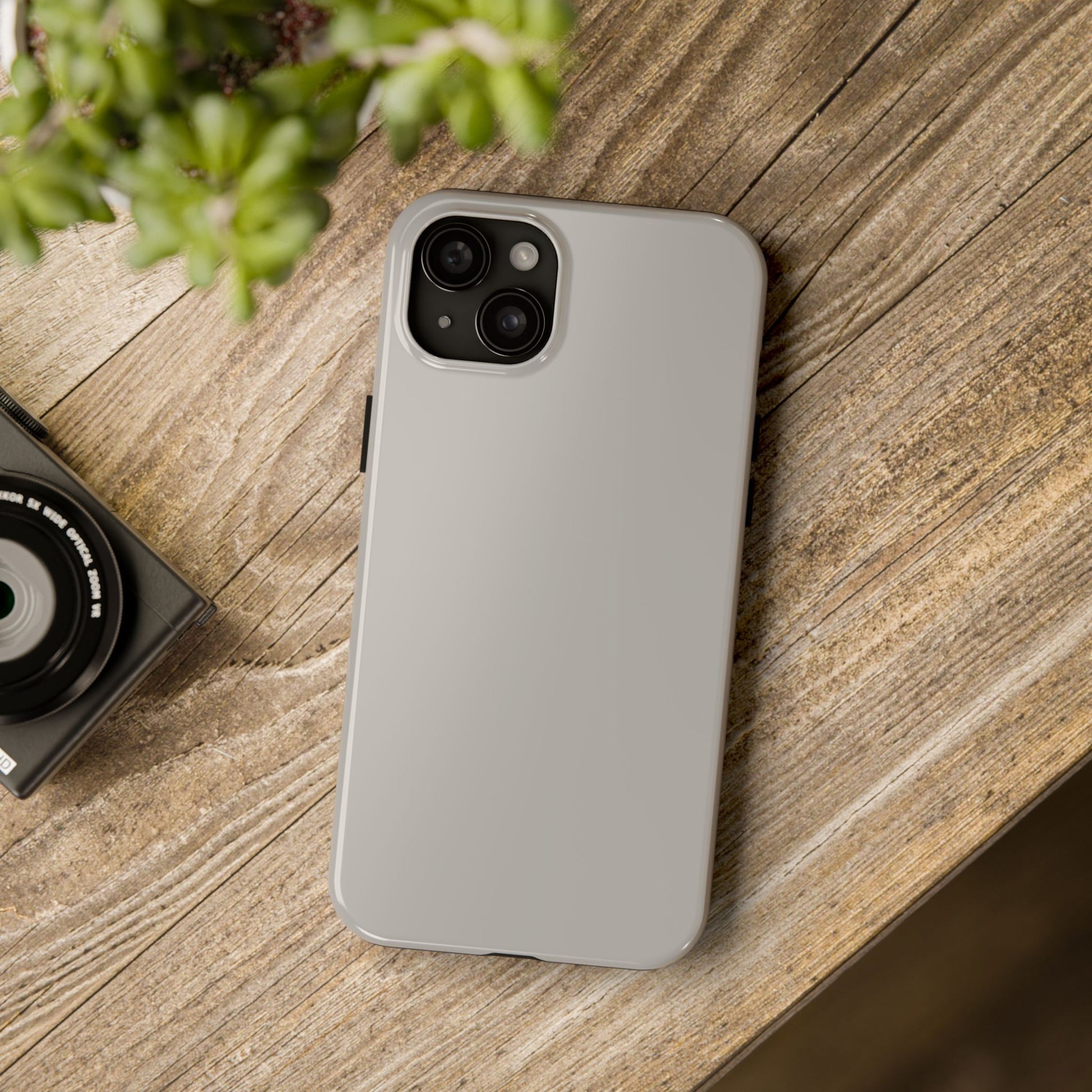 iPhone 15 Plus Aston Martin Silver Birch phone case on a table with accessories. 