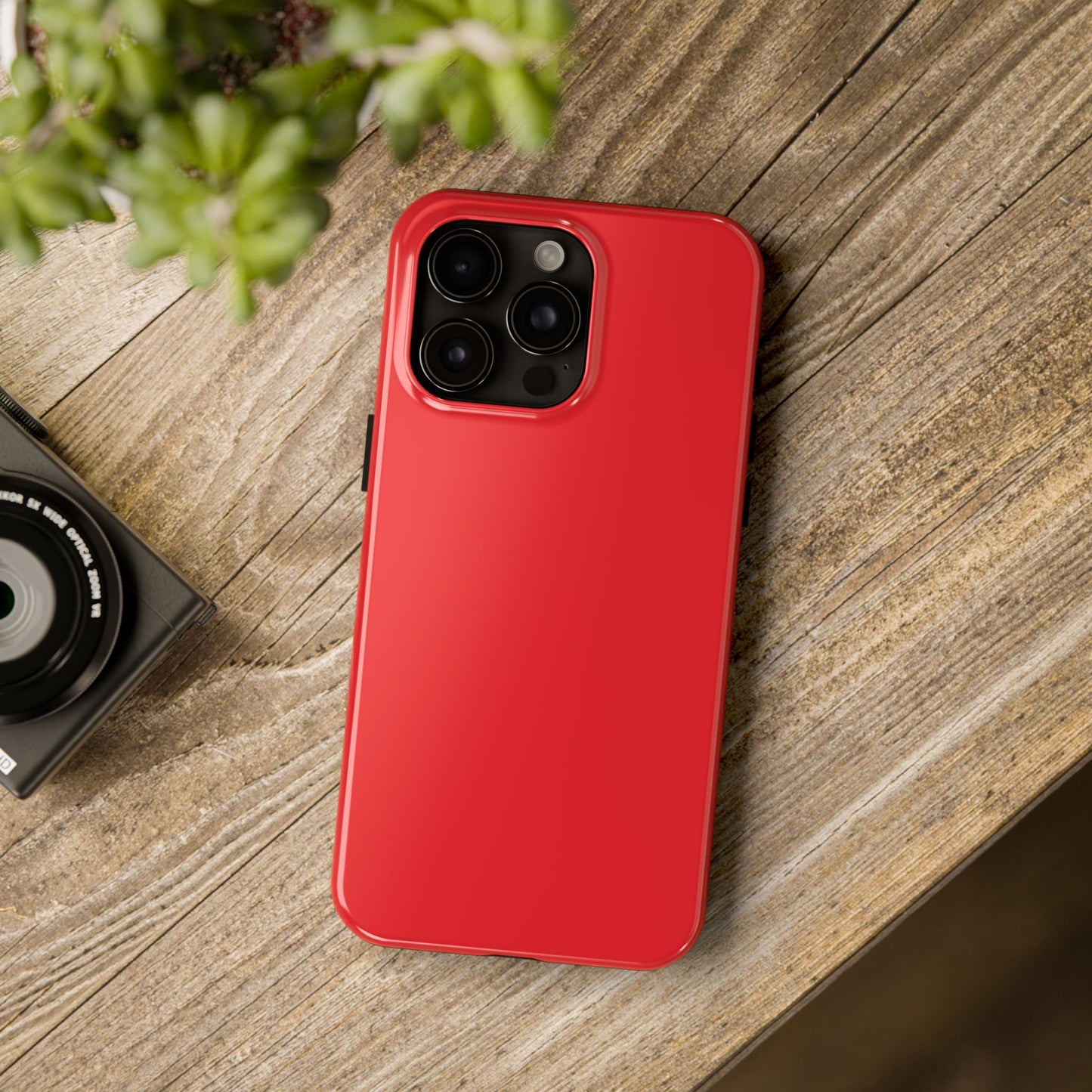 iPhone 15 Pro Max Aston Martin Volcano Red phone case on a table with accessories. 