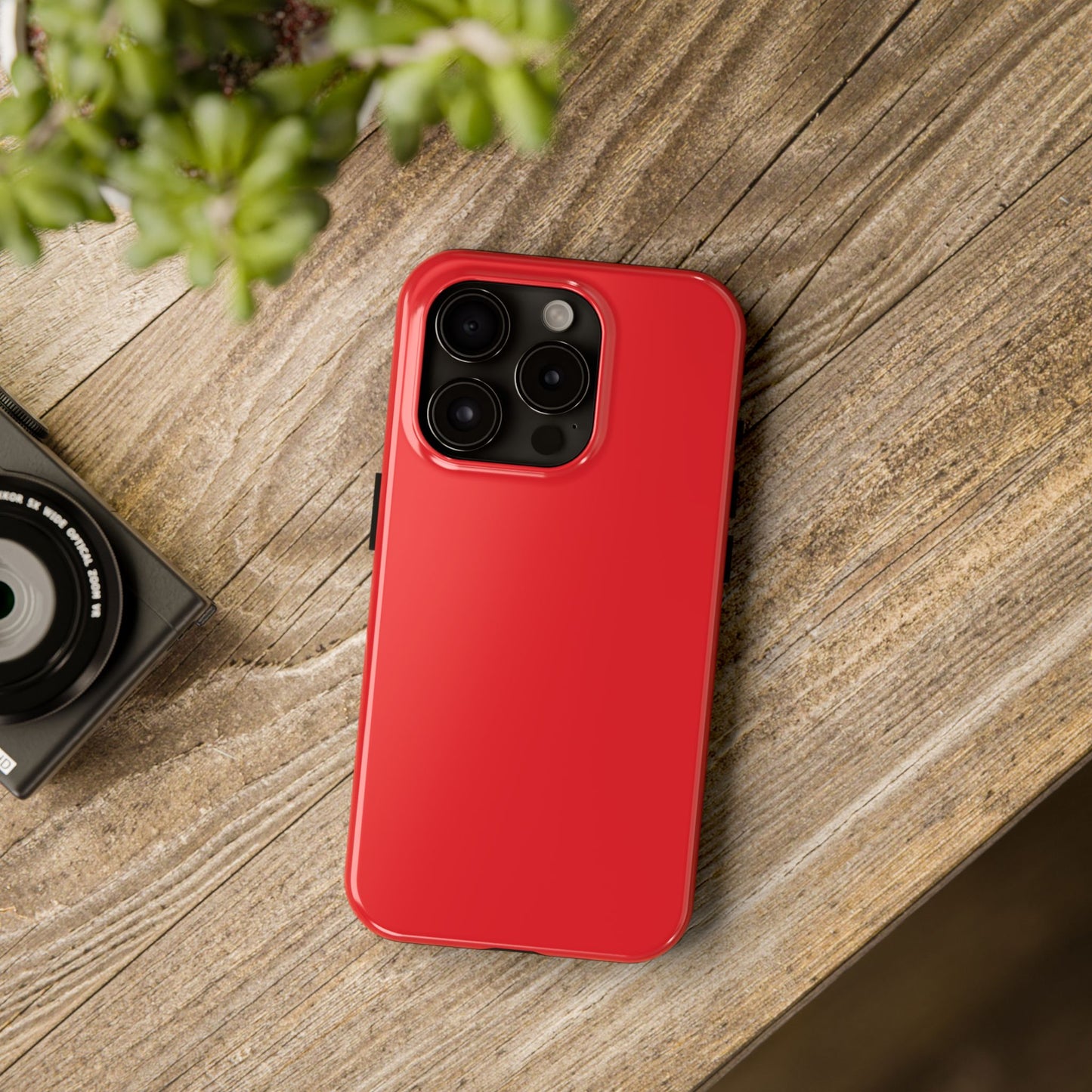 iPhone 15 Pro Aston Martin Volcano Red phone case on a table with accessories. 