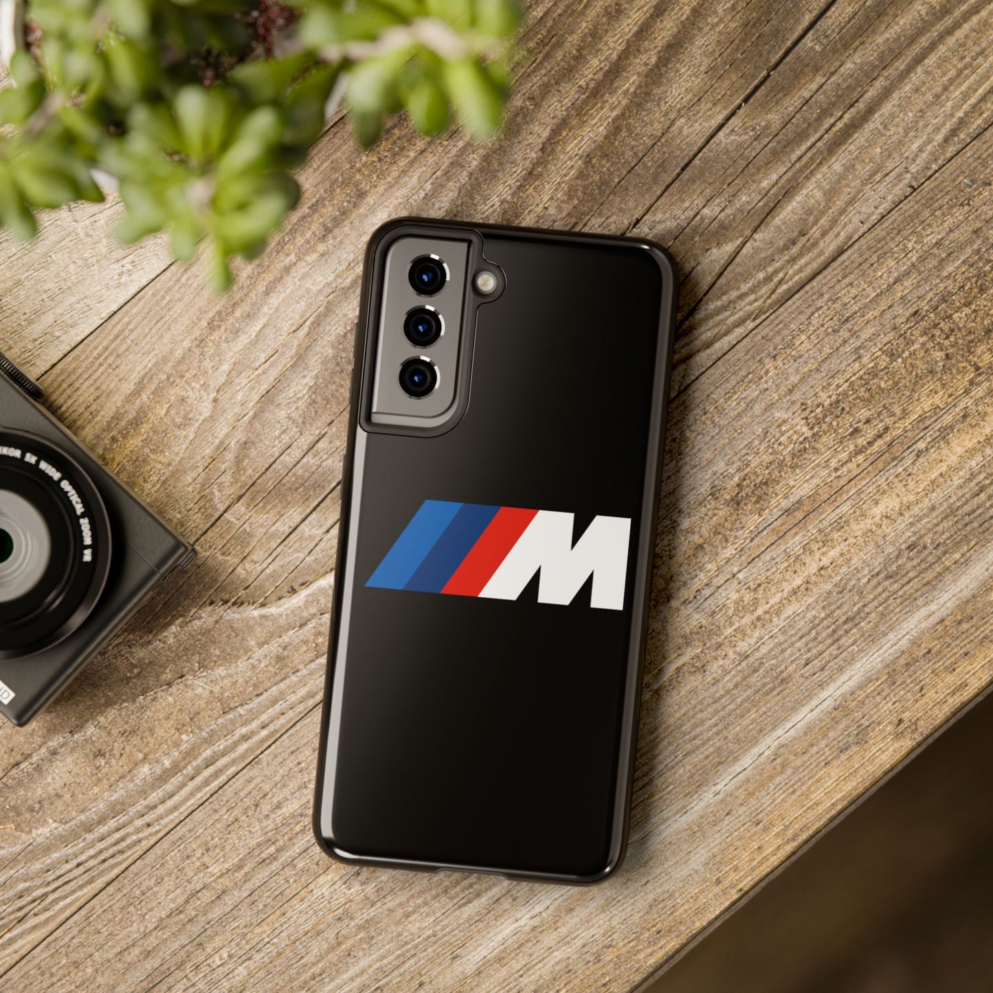 Black Samsung S21 BMW M phone case on a table with accessories.