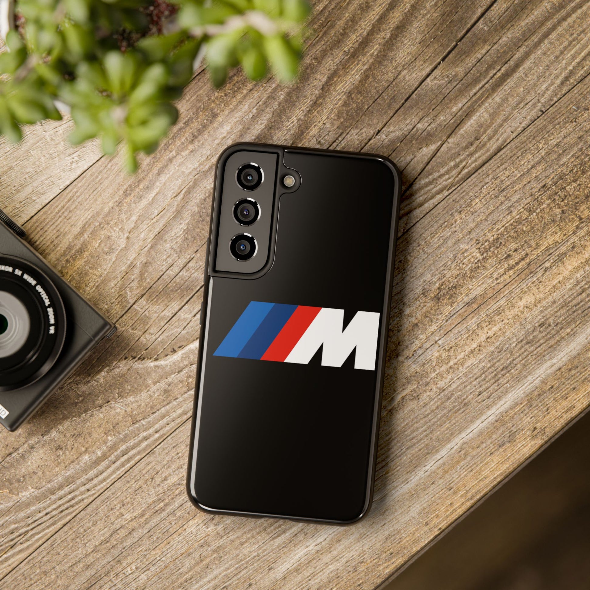 Black Samsung S22 BMW M phone case on a table with accessories.