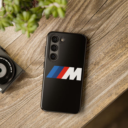 Black Samsung S23 BMW M phone case on a table with accessories.