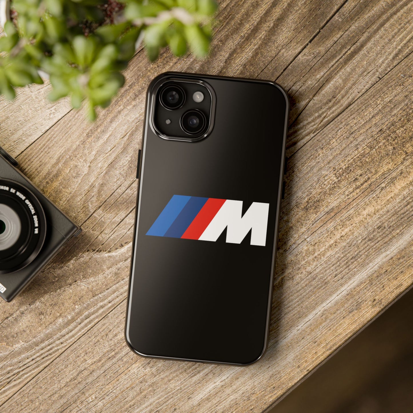 Black iPhone 15 Plus BMW M phone case on a table with accessories.