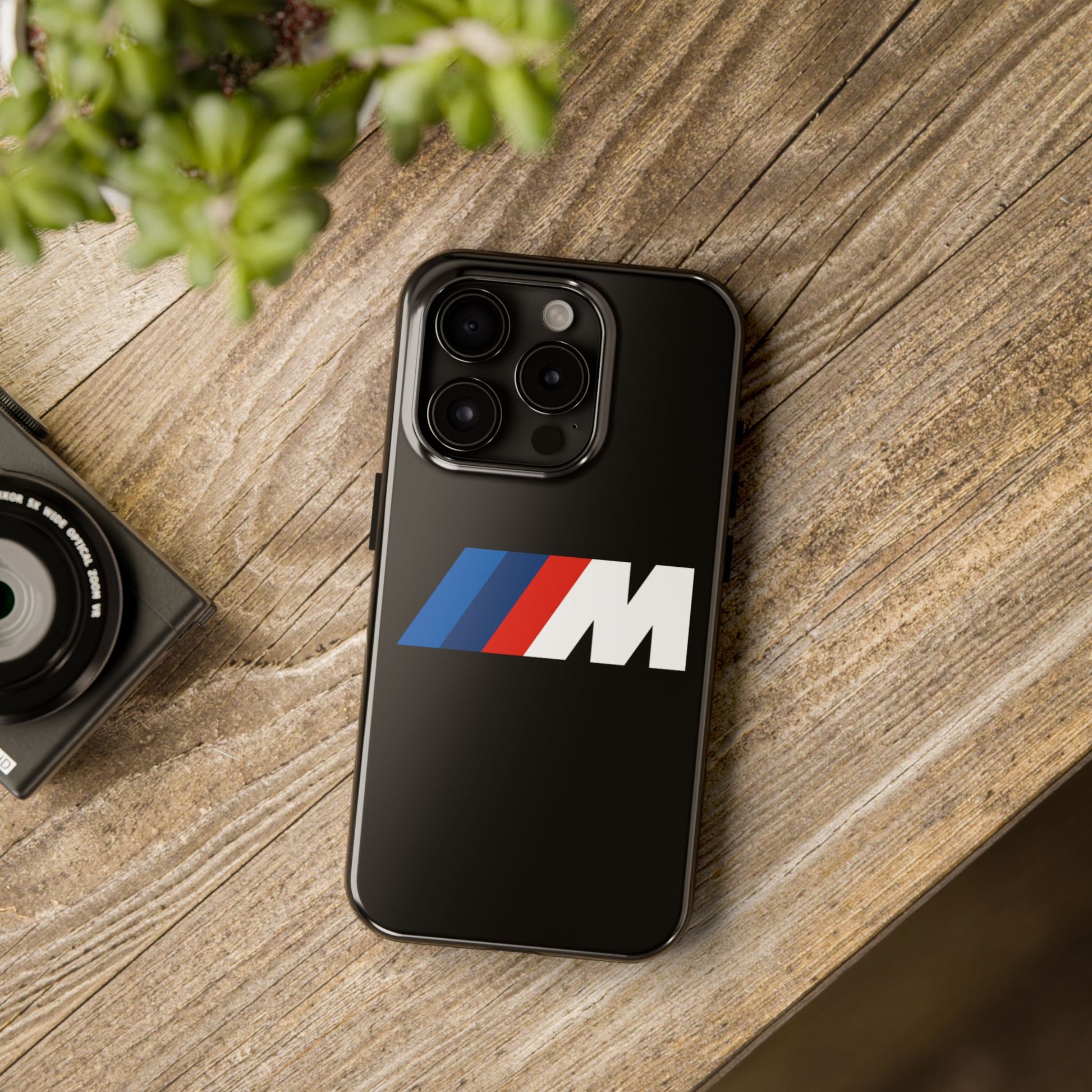 Black iPhone 15 Pro BMW M phone case on a table with accessories.