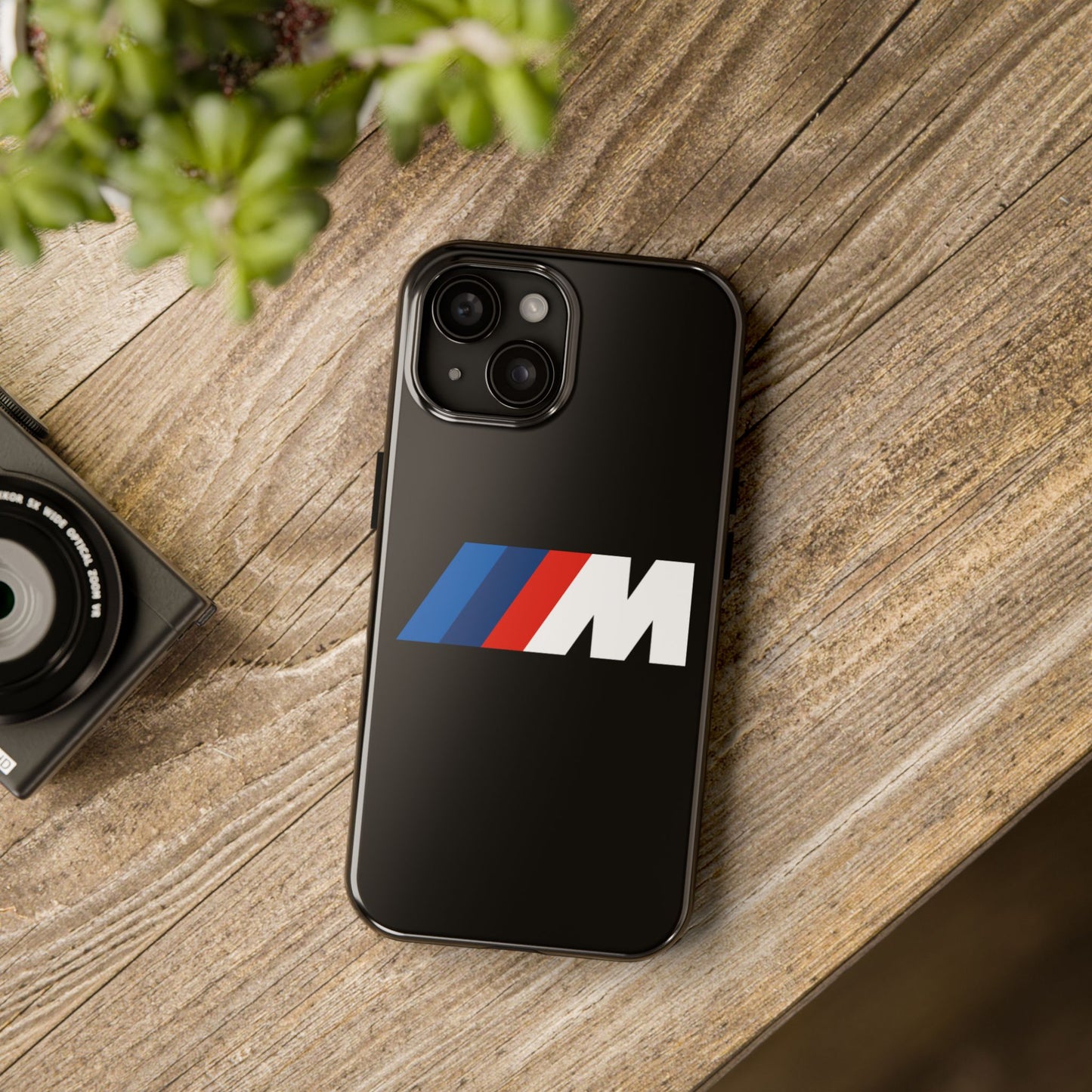 Black iPhone 15 BMW M phone case on a table with accessories.