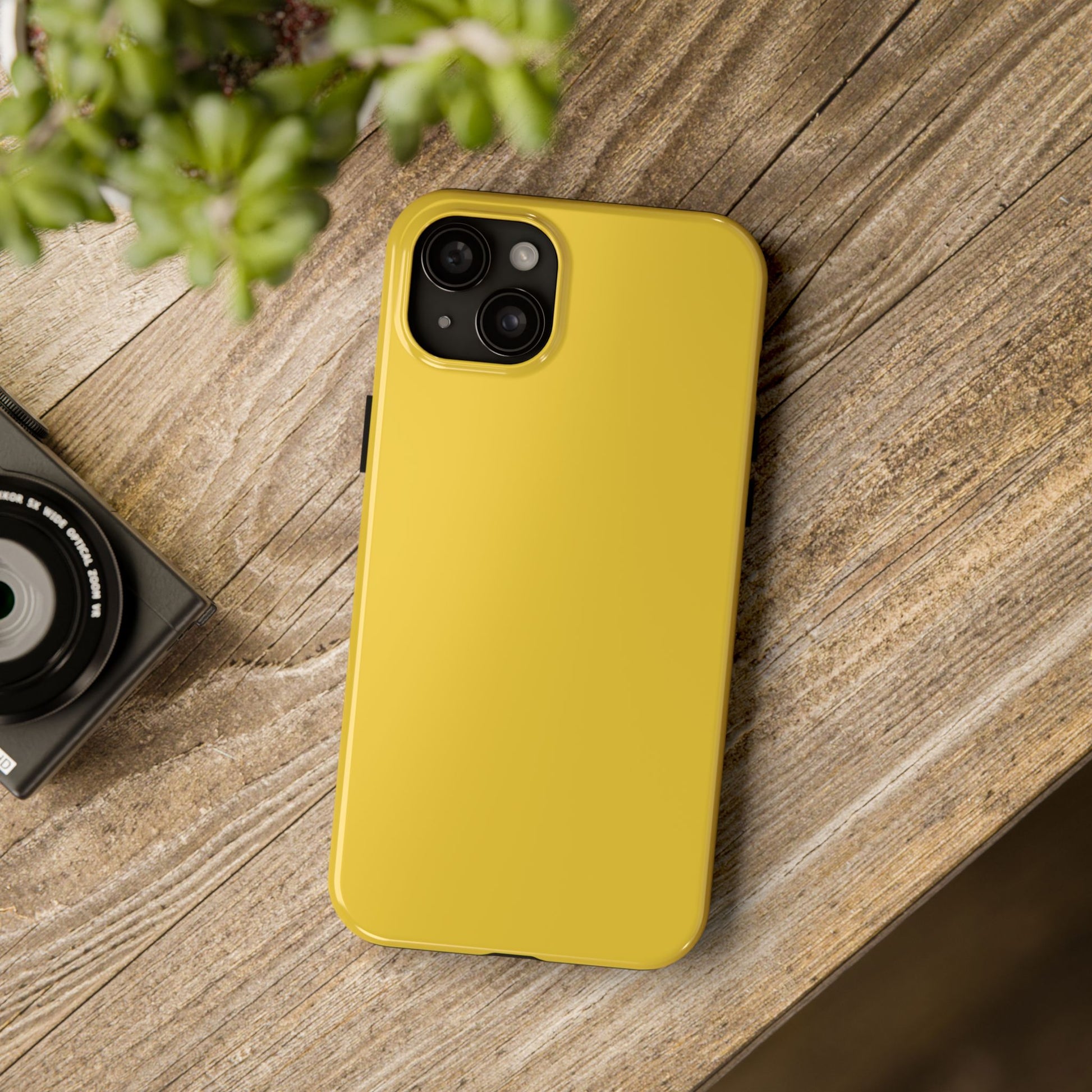 iPhone 15 Plus Porsche Speed Yellow phone case on a table with accessories. 