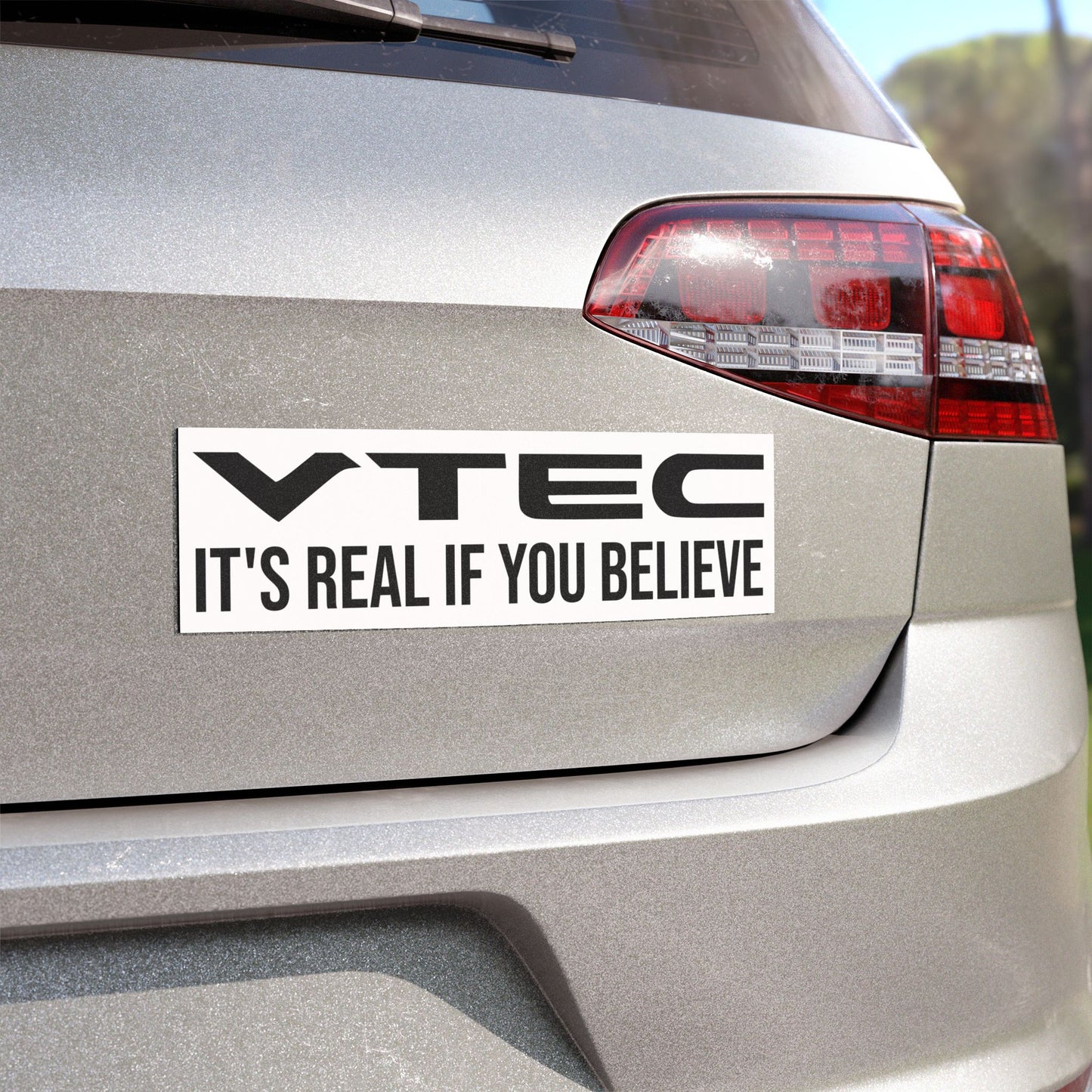 White with Black text on an Angled view of the VTEC It's Real If You Believe Magnet on the rear end of a car